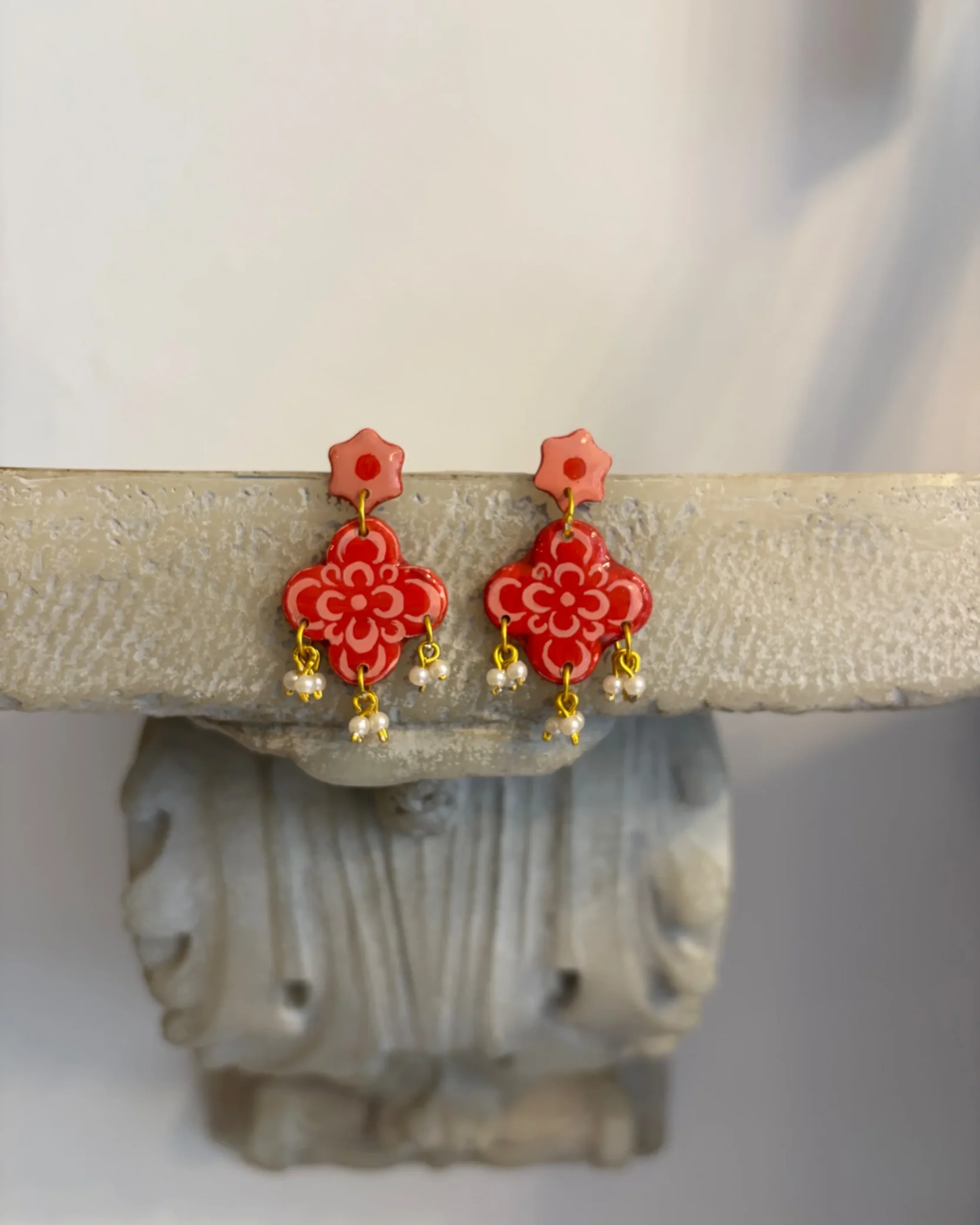 Coral pink tile-pattern flower earrings with pearl drops, on a stone shelf