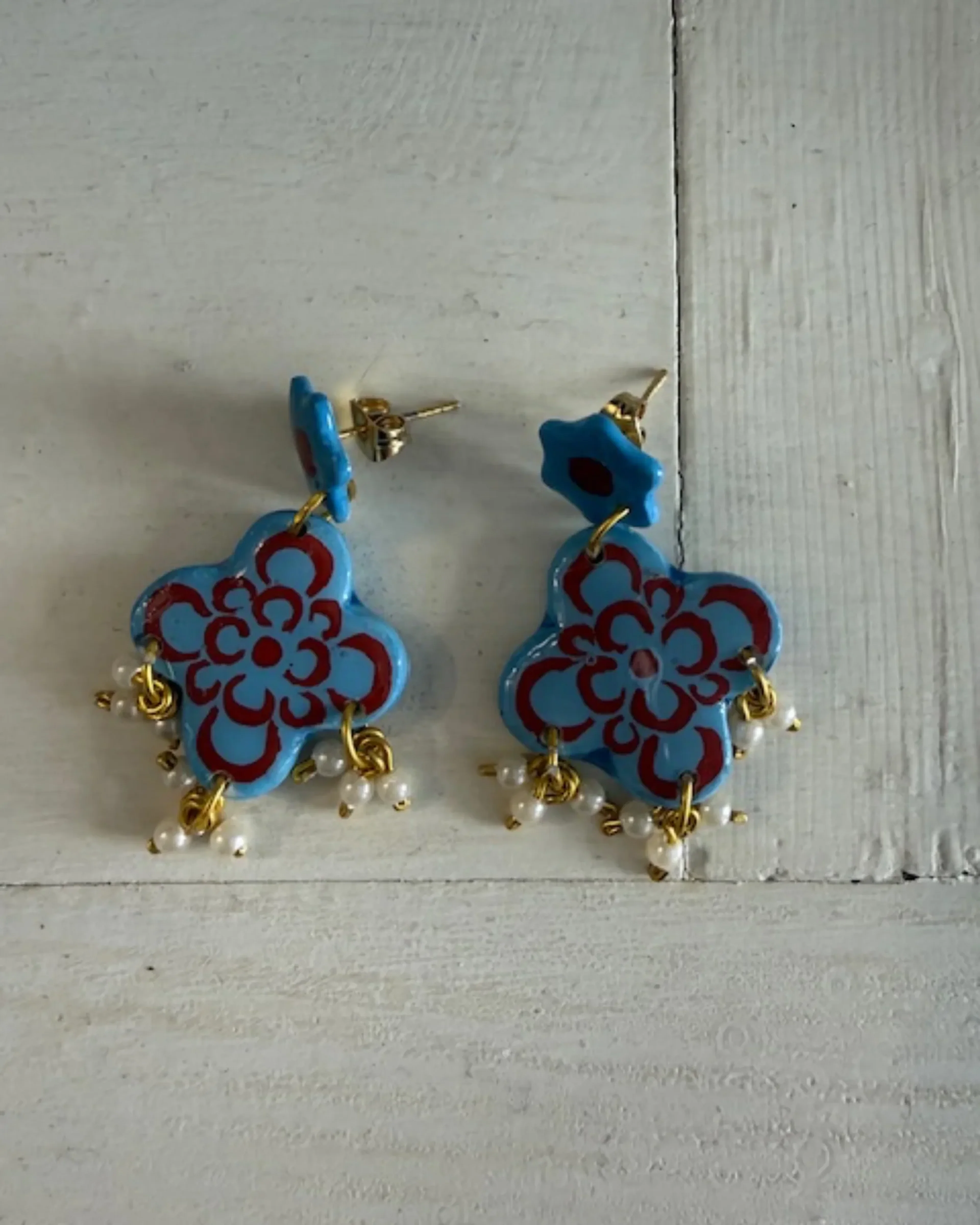 Silver-blue and burnt orange tile-pattern flower earrings on a pale wood backdrop